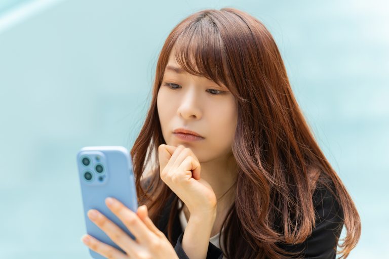 スマートフォンを手に考えこむ女性
