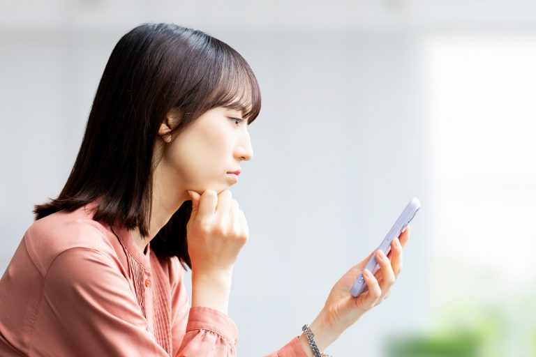 スマートフォンを見ながら悩む女性